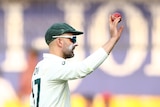 Nathan Lyon holds up a red cricket ball