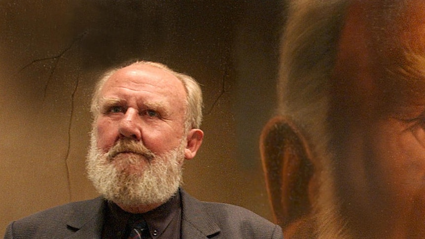 Bill Hunter standing in front of his portrait by Jason Benjamin for the Archibald.