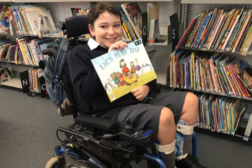 School boy in a wheelchair, holding a book.