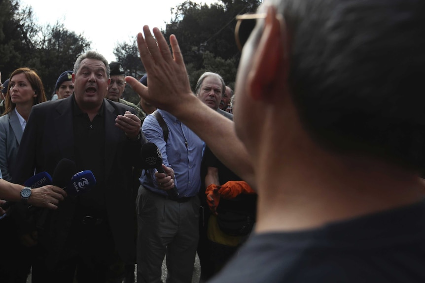 A local resident holds his hand up as he argues with the Greek Defence Minister.