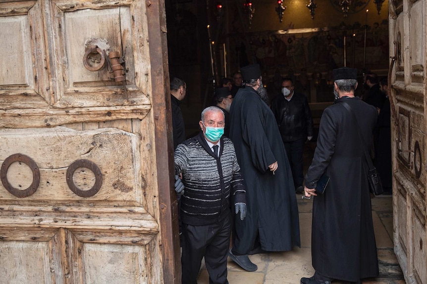 Wajeeh Nuseibeh wearing face mask closing doors to the Holy Sepulchre, with religious leaders dressed in black inside.