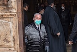 Wajeeh Nuseibeh wearing face mask closing doors to the Holy Sepulchre, with religious leaders dressed in black inside.