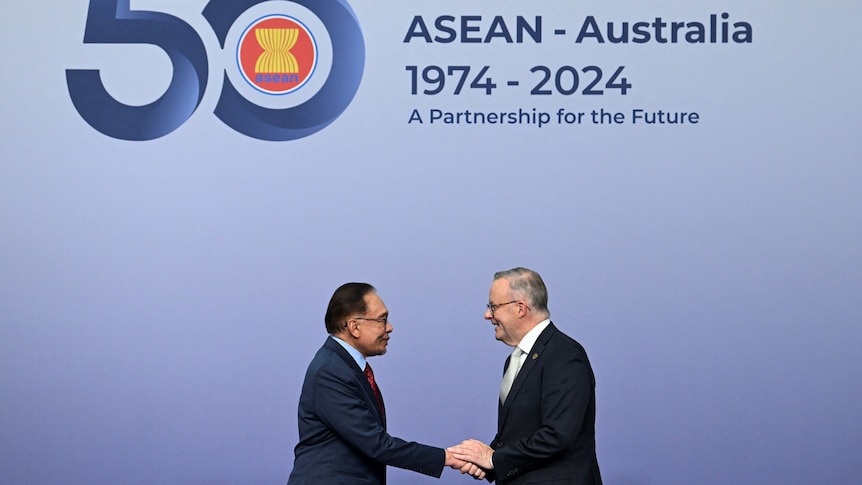 Anthony Albanese shakes hands with a shorter Asian man in front of a 50 years ASEAN sign