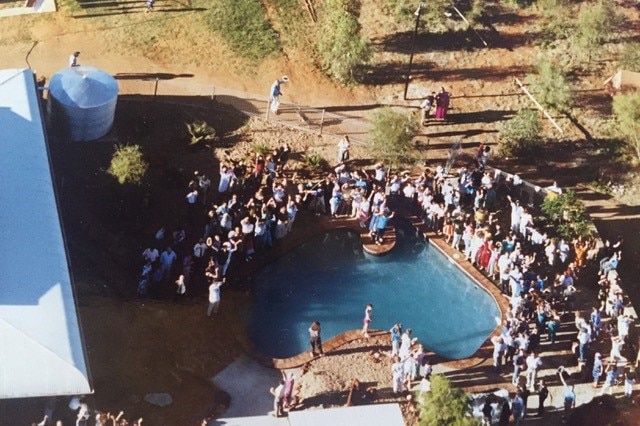 An older photo with an aerial view of a group of people gathered around an Australia-shaped pool, having a party.