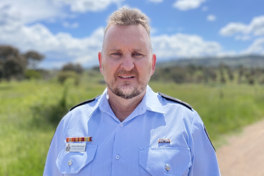 Shawn smiles, wearing his uniform and standing outside in the sun.