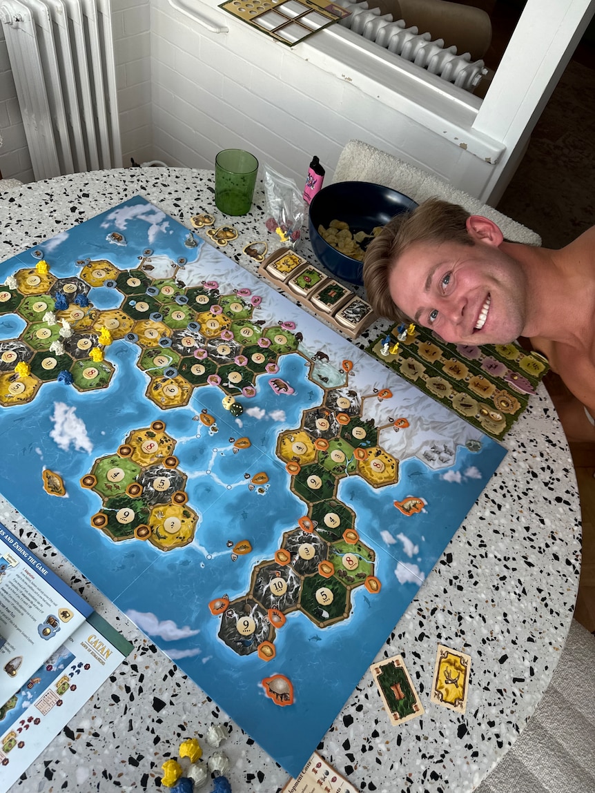 Tim Abbott poses for a photo with Catan, a board game, part of a regular games night with friends with snacks
