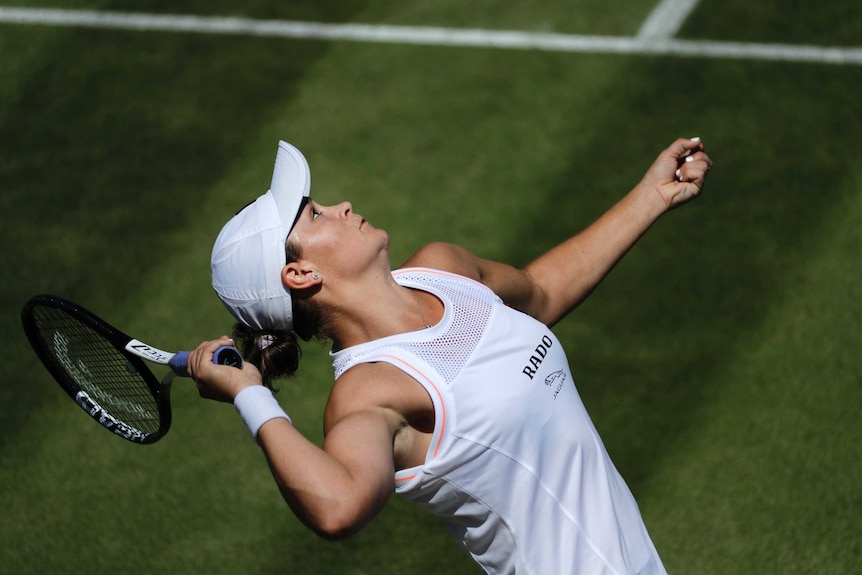 A female tennis player holds a racquet behind her head as she prepares to serve a tennis ball.