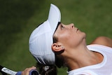 A female tennis player holds a racquet behind her head as she prepares to serve a tennis ball.