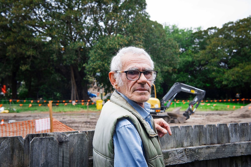 Elder Uncle Des next to the light rail site where an excavator is digging.