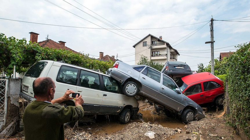A man takes a photo of damaged vehicles following floods in the village of Stajkovci
