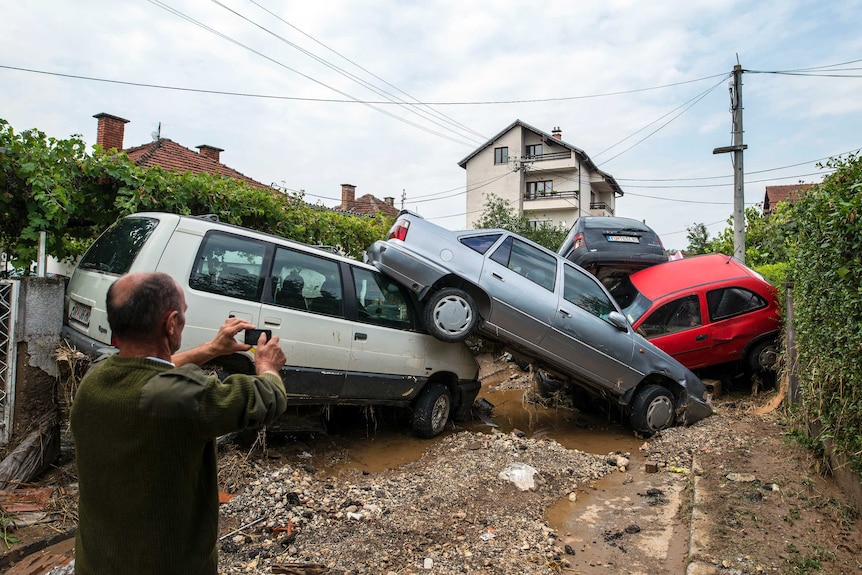 A man takes a photo of damaged vehicles following floods in the village of Stajkovci