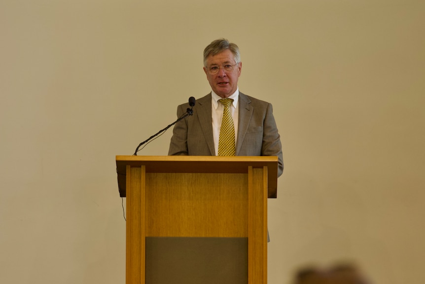 A man in a suit stands at a lectern.
