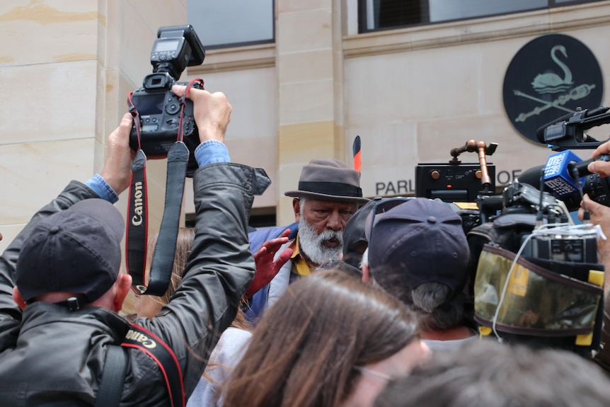 Ernie Dingo is flanked by media on the steps of WA Parliament