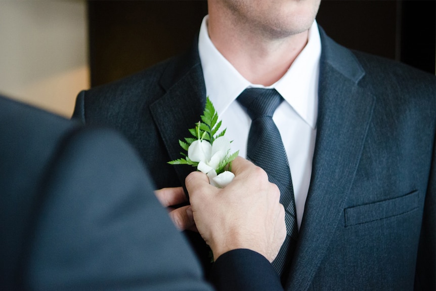 A groom has a boutonniere pinned to his suit jacket.