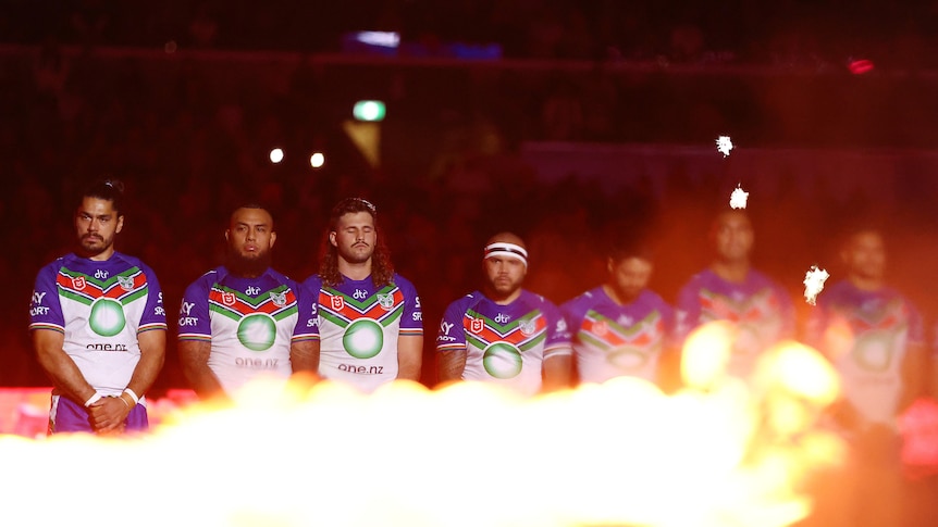 NRL players standing for a minute silence, as a flame burns in front of them during an Anzac ceremony