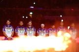 NRL players standing for a minute silence, as a flame burns in front of them during an Anzac ceremony