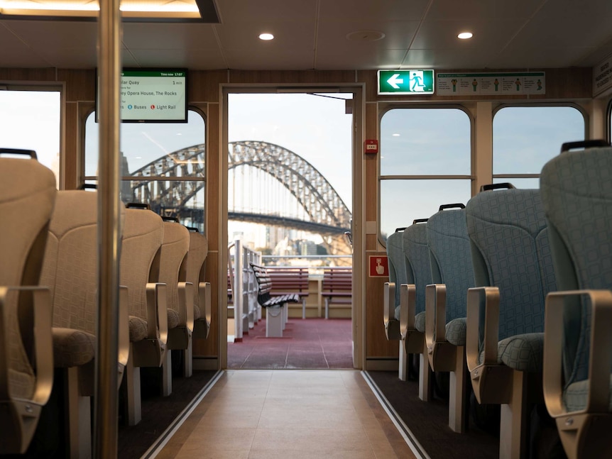 Empty rows of seats on either side of the aisle, the Sydney Harbour Bridge visible through the door