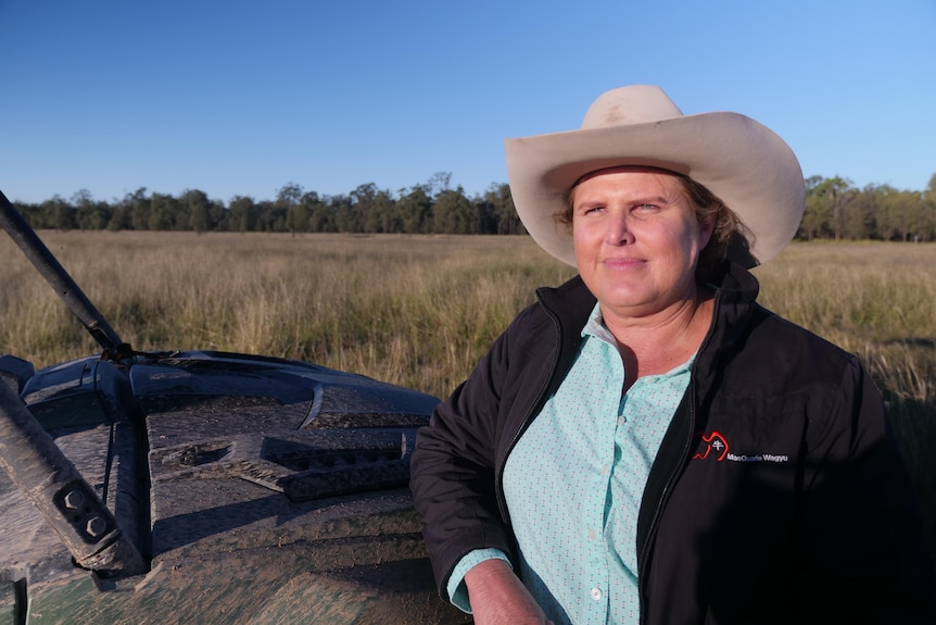 A woman in a broad-brimmed hat and dark jacket, standing on a farm.