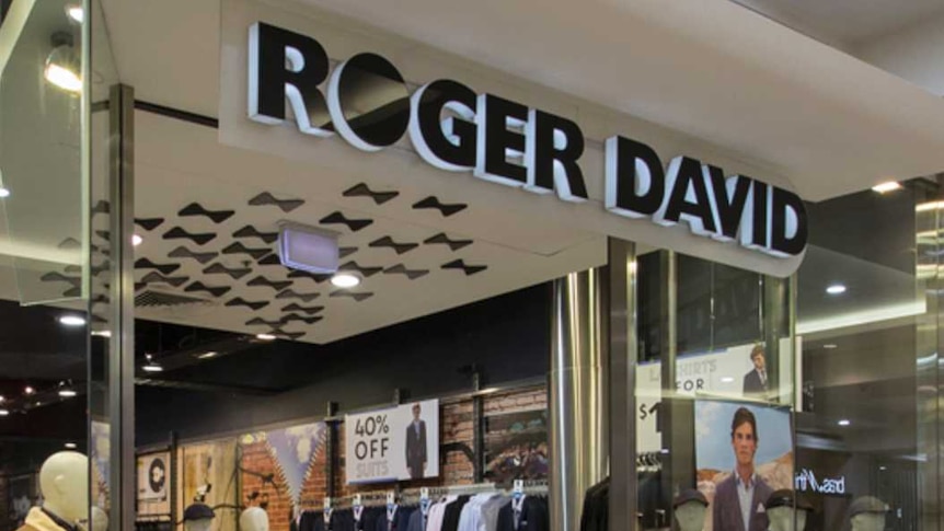 Six dummies dressed in menswear stand in the window of a store with a 'Roger David' sign