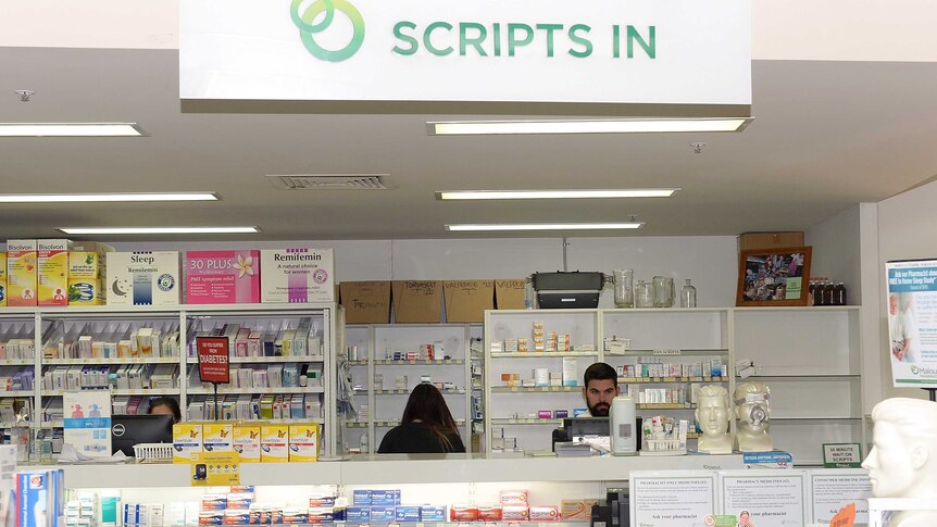 Three pharmacists at work behind a white counter lined with products.
