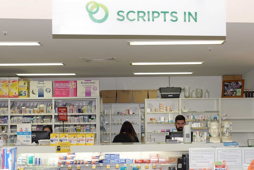 Three pharmacists at work behind a white counter lined with products.