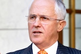Upper body photo of Malcolm Turnbull gesturing as he speaks at a podium during a press conference.