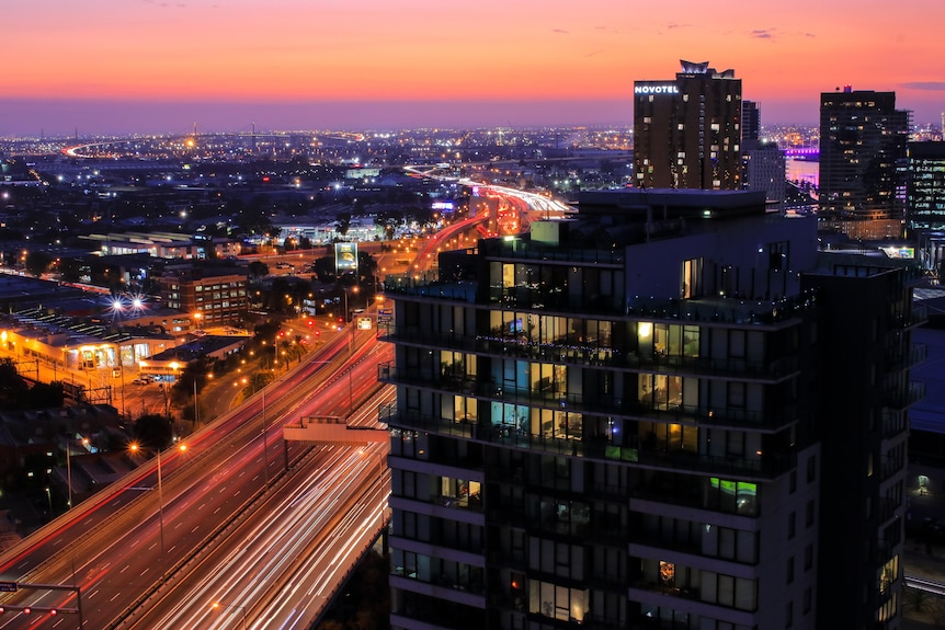 A sunset picture looking over high-rise apartment next to freeway with blured lights of traffic