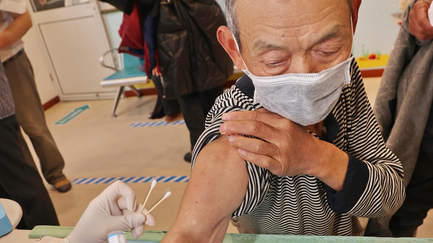 A Chinese man rolls up his sleeve to receive a vaccine 