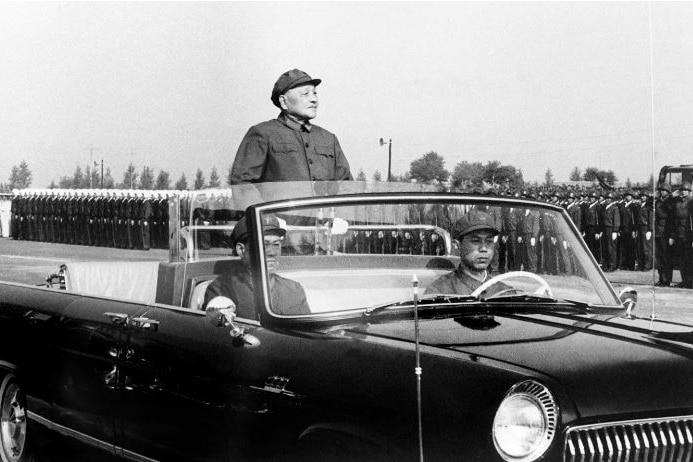 Une photo en noir et blanc de Deng Xiaoping dans une voiture avec le toit ouvert.