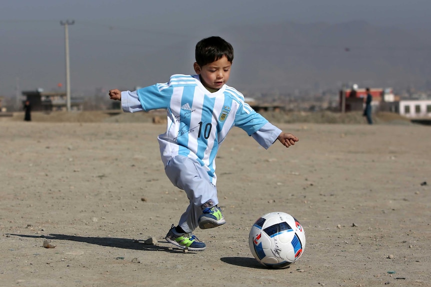 Afghan boy Murtaza Ahmadi plays with a ball in Kabul while wearing a shirt signed by Lionel Messi.
