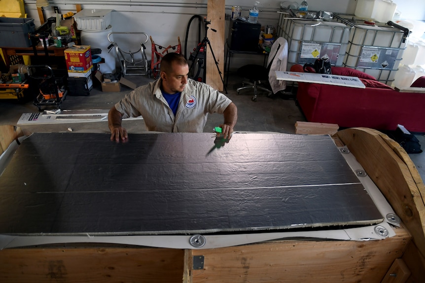 A man works on a nearly completed human body composting vessel closing it off with a black board 