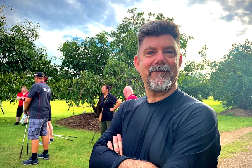 A portrait style photo of an older man with a beard, standing on a golf course.