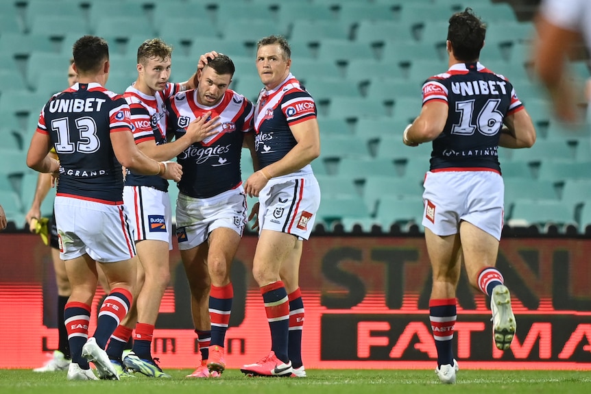 NRL players surround a tryscorer, patting his head and putting their arms around him.