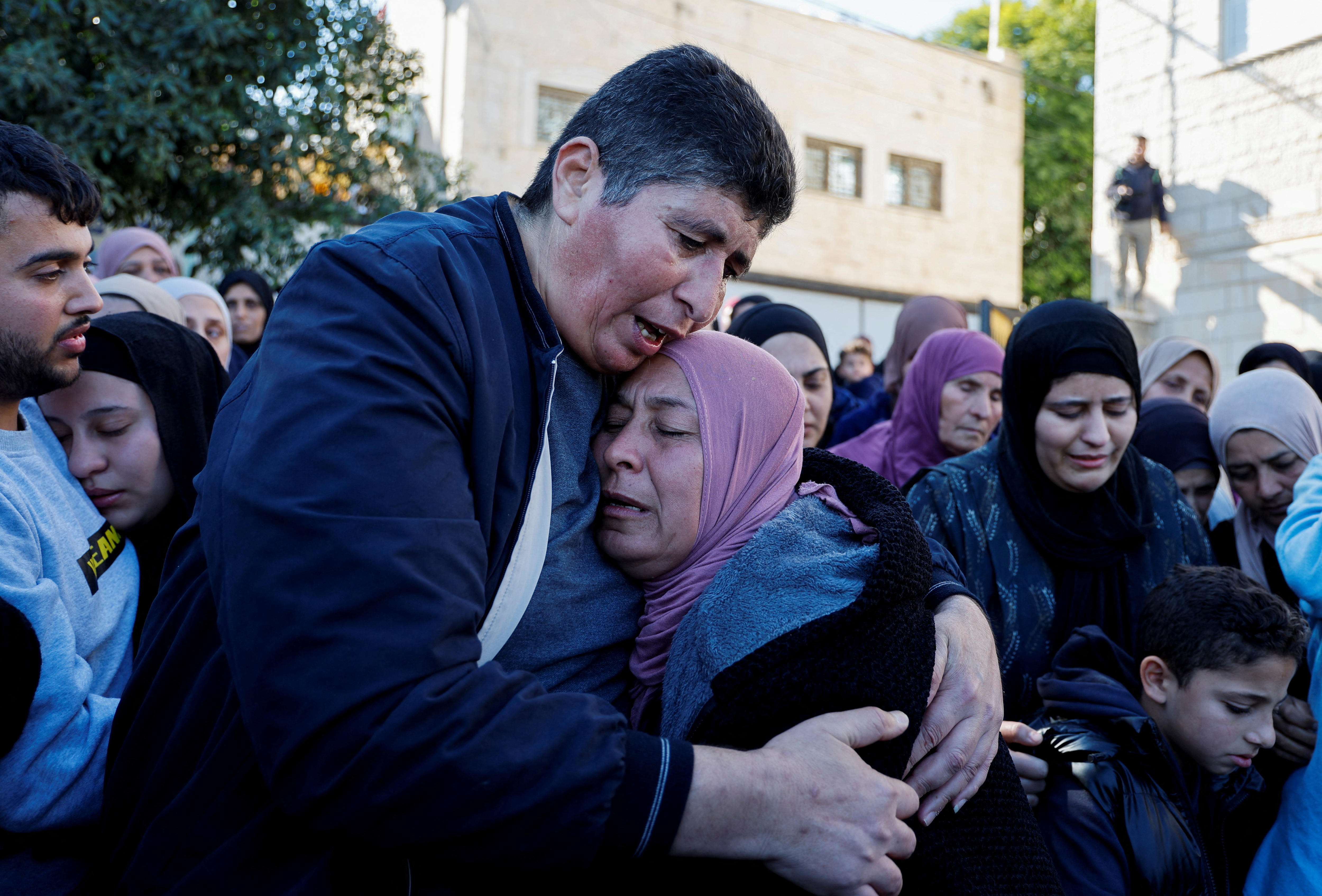 A crowd of people hug each other with their eyes closed.