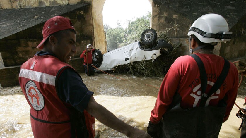 Rescue workers look at a car stuck underneath a bridge after heavy rains in Oaxaca state