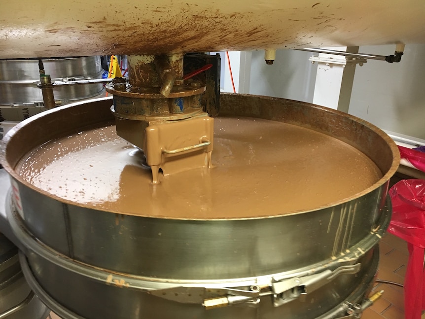 Chocolate is stirred in a large metal vat.