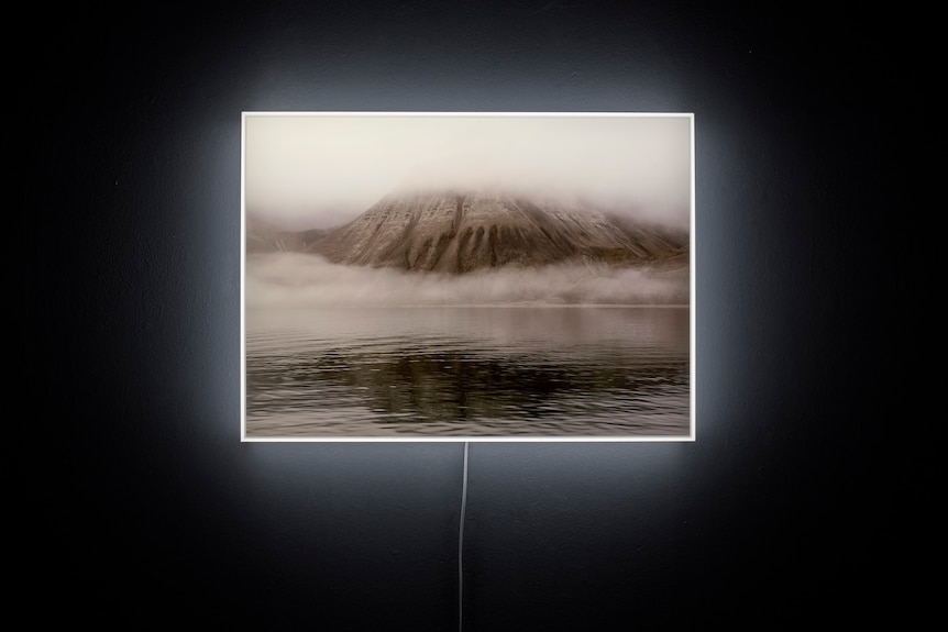 A black and white mountain landscape, obscured by fog, displayed on backlit film.