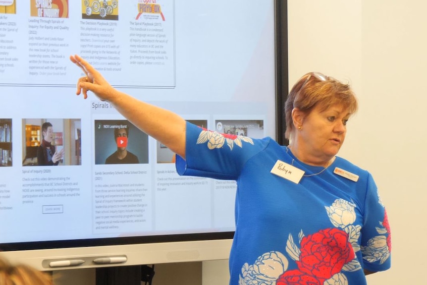 Robyn Thorpe points two fingers at a powerpoint slide titled "Closing Reflections" while talking to a class.