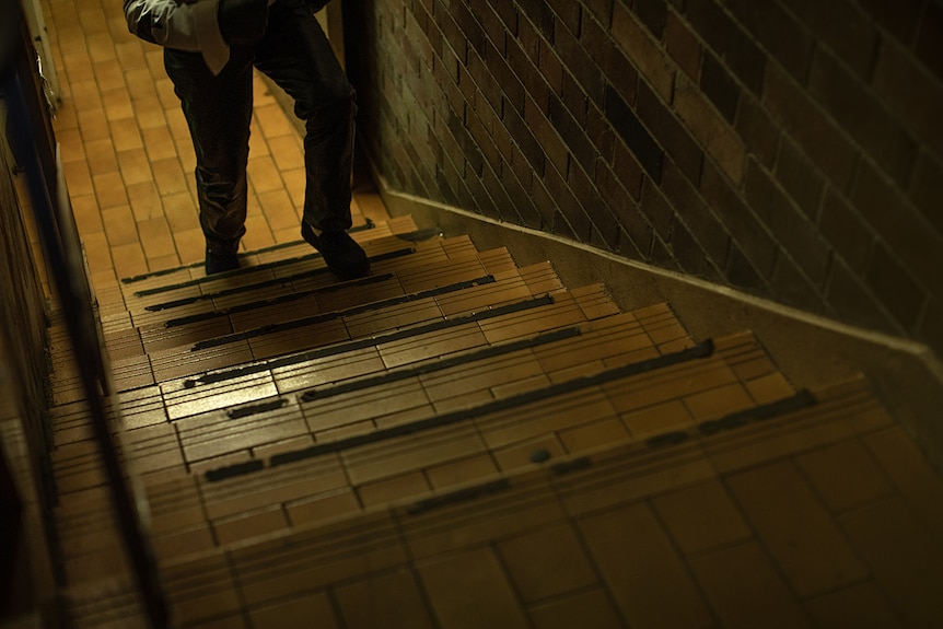 A man, who is cut off from the waist down in the photo, walks up a set of stairs