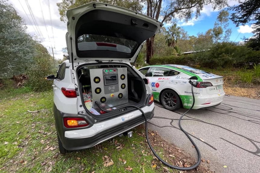 An EV recharging via a cable from the back of another car