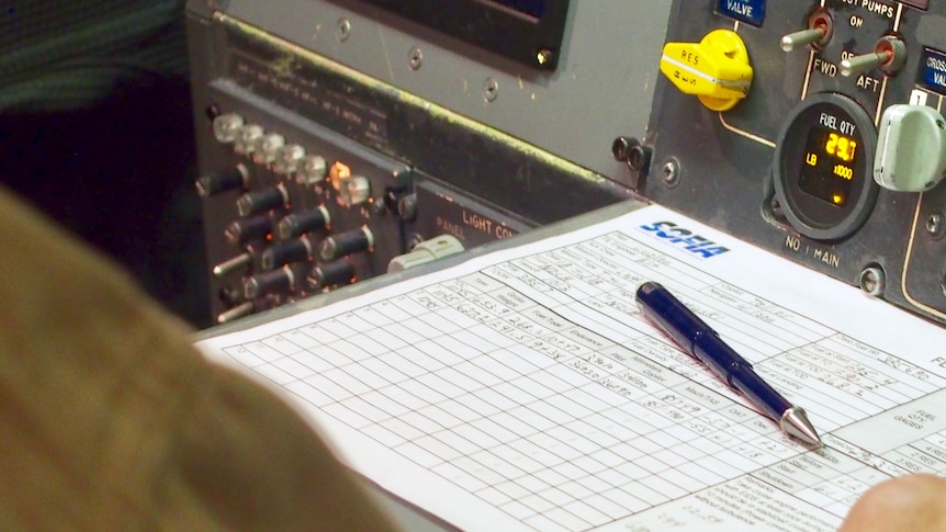 A paper chart titled "Flight engineer's fuel log" sits on a shelf next to a panel covered in switches and dials.