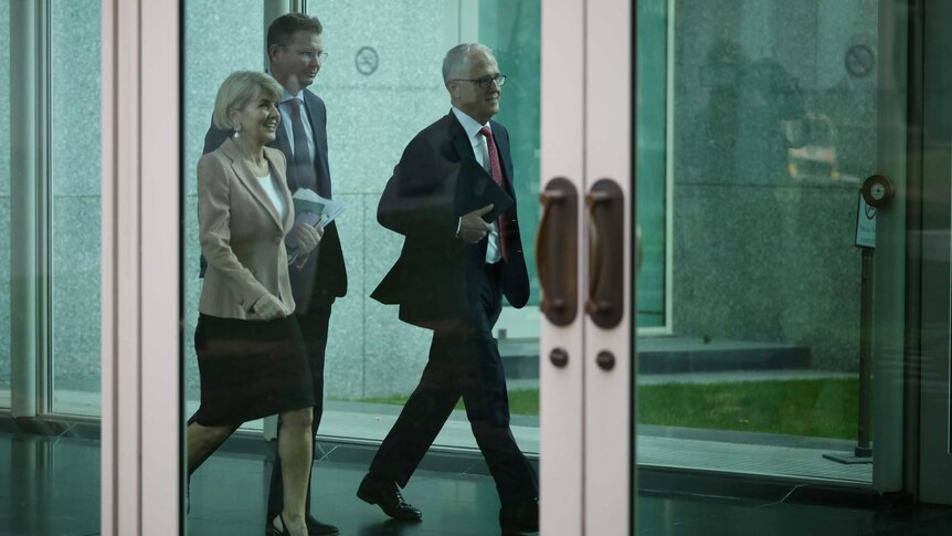 Malcolm Turnbull and Julie Bishop walk side by side, Ms Bishop smiling, down a corridor with another man