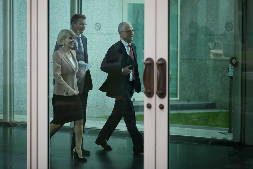 Malcolm Turnbull and Julie Bishop walk side by side, Ms Bishop smiling, down a corridor with another man