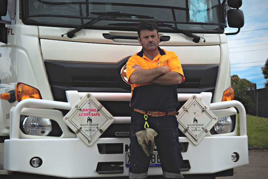 Man wearing hi-vis standing with his arms folded in front of a large truck.