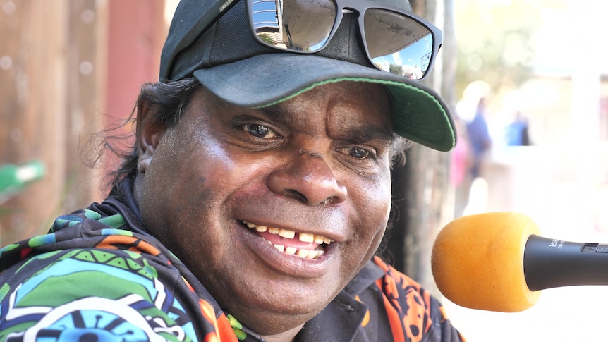 Close up photo of Indigenous man smiling in front of microphone.