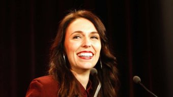 New Zealand's Labour Party leader Jacinda Ardern smiles under bright lights at a podium