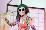 A Japanese Australian woman dressed in eclectic clothing and large sunglasses performs onstage.