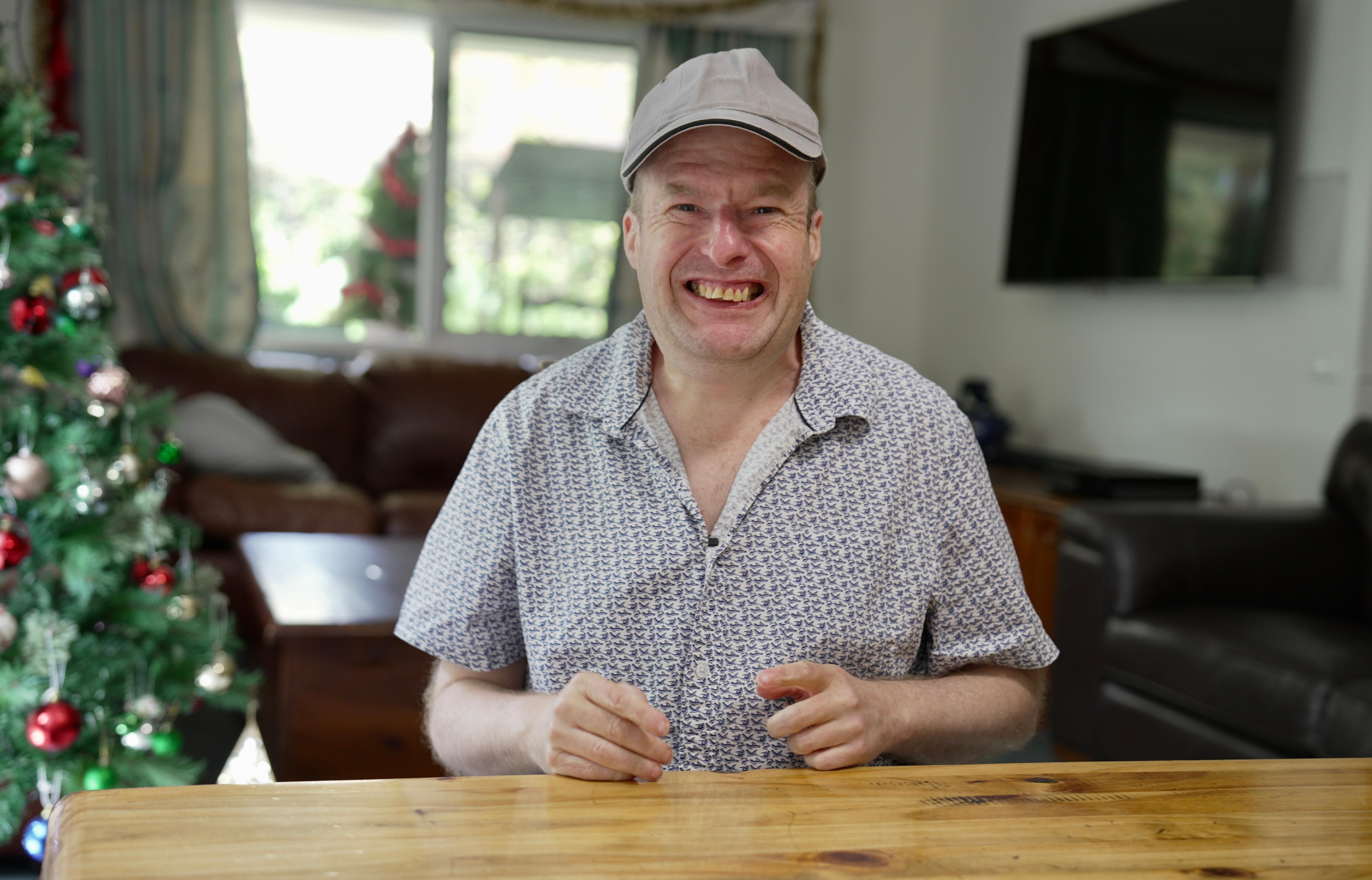 Un hombre y una mujer se sientan uno al lado del otro en una mesa de madera del parque y sonríen.