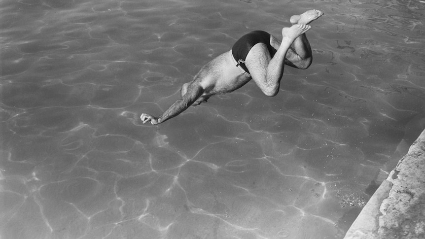 A black and white photo of a man leaping into a pool.