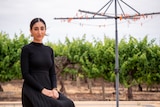 Simi Gill sits on a chair near a clothesline with grape vines in the background near Barmera, South Australia, November 2023.